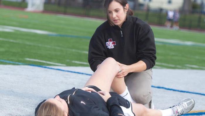 An athletic training student stretches an athlete's leg on a field.