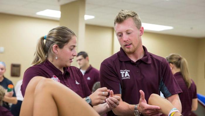 Two athletic training students working on a client's arm in an athletic training facility.
